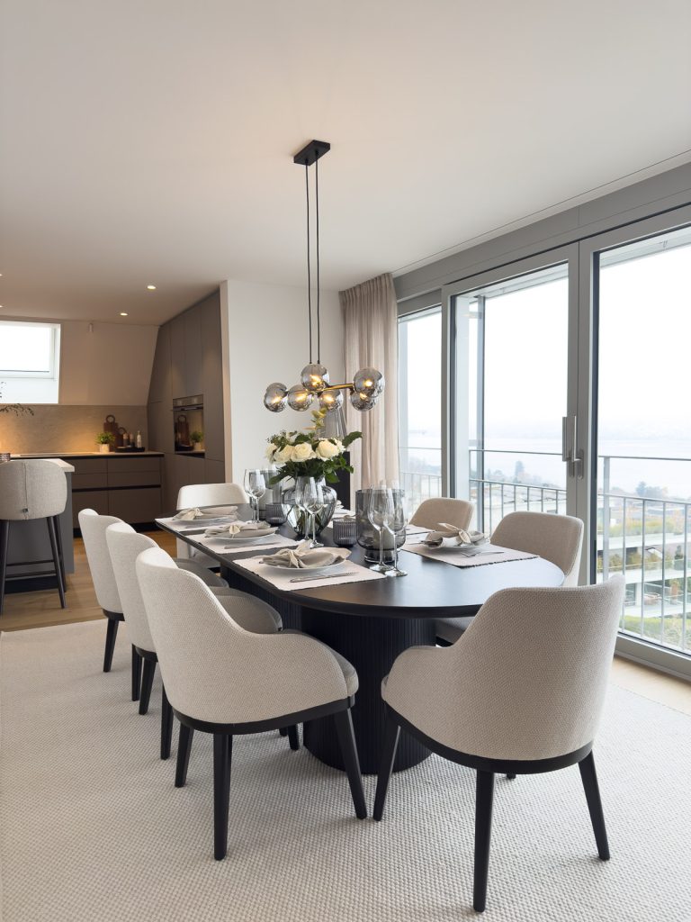 Modern dining area with oval table, upholstered chairs and designer pendant lighting in an open-plan apartment